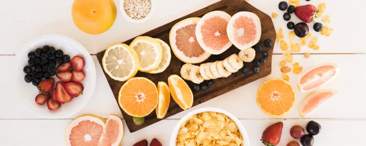 Assorted sliced citrus fruits, berries, and cereal highlight nutrition and ingredients on a white table with a wooden board. | Emping SG