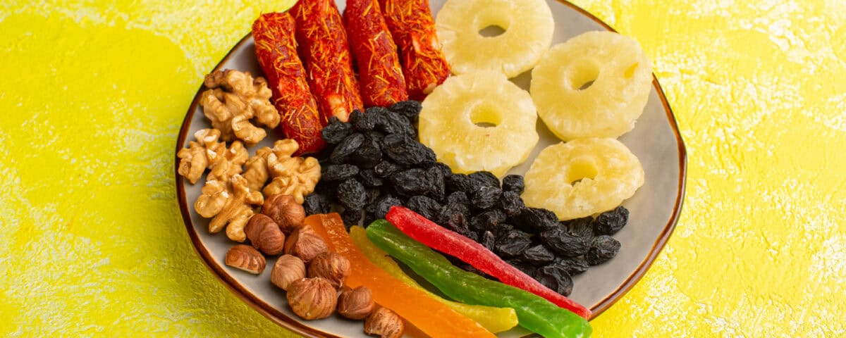 A plate with Premium Fruit Snacks: dried pineapple rings, nuts, berries, and fruit rolls on a yellow background. | Emping SG