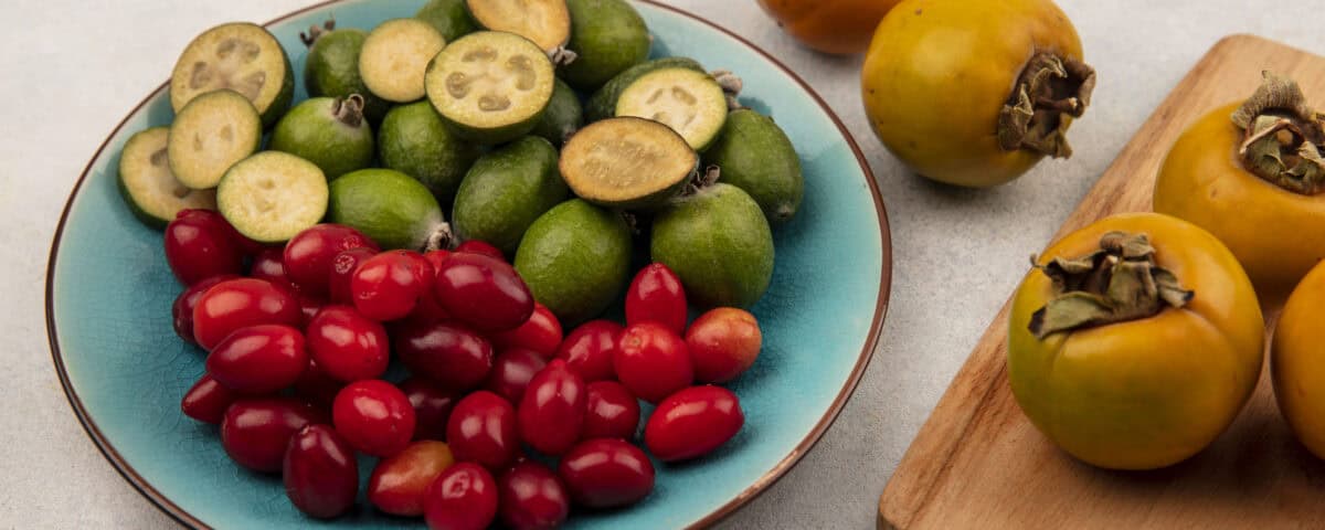 A blue plate with feijoas, red berries, and Emping Melinjo crackers next to yellow persimmons on a wooden board. | Emping SG