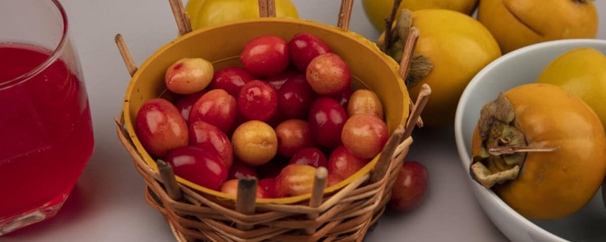 A wicker basket of red cherries, Emping Melinjo chips, and yellow persimmons on a gray surface. | Emping SG