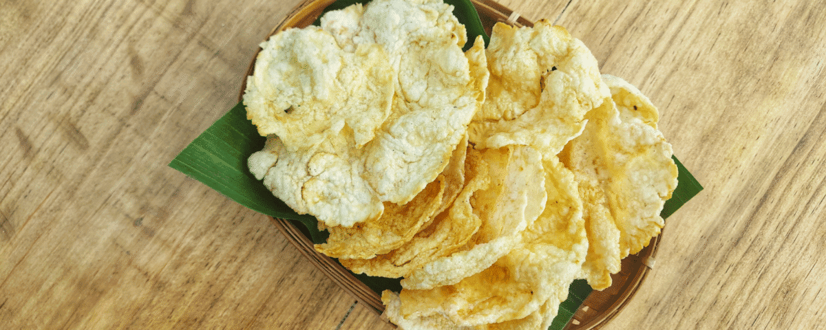 A plate of crispy Emping Crackers with a hint of bitter flavour on a green leaf, placed on a wooden table. | Emping SG