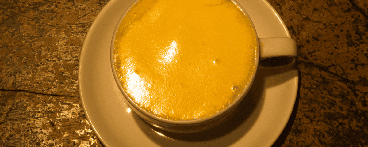 A cup of golden yellow Egg Coffee with frothy top, served on a white saucer in Hanoi Old Quarter. | Emping SG