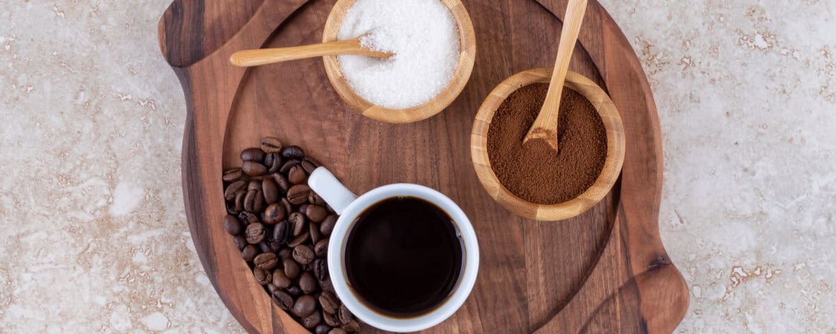 Cup of black coffee, coffee beans, sugar, and ground coffee on a wooden tray—explore the health benefits from above. | Emping SG