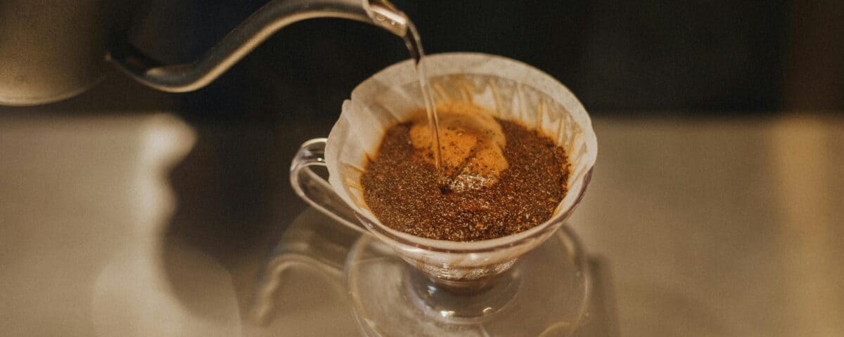 Hot water poured over ground coffee in a glass pour-over dripper for fresh flavour—your guide to Vietnam Drip Coffee. | Emping SG