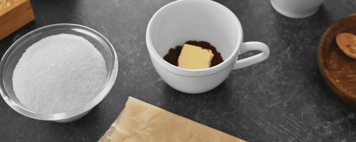 A cup with cocoa powder and butter, a bowl of sugar, and baking ingredients on a dark worktop. | Emping SG