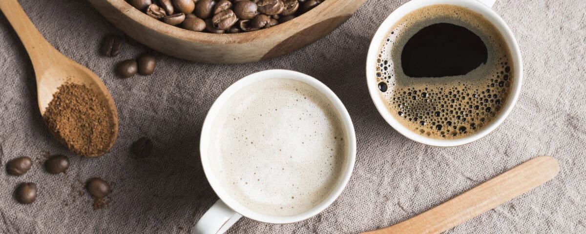 Two cups of coffee, coffee beans, ground coffee, and sugar on a textured cloth with wooden spoons and bowl. | Emping SG