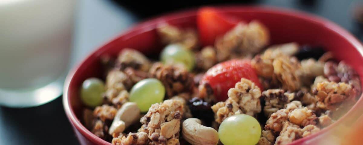 A red bowl filled with high-fibre snacks like granola, grapes, nuts, and strawberries sits next to a glass of milk. | Emping SG