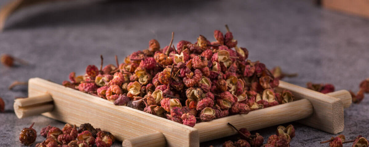 A pile of dried Sichuan peppercorns on a small wooden tray, with some scattered on a grey surface. | Emping SG