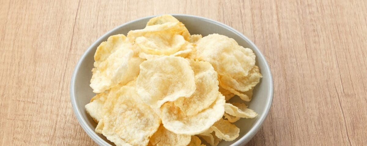 A white bowl filled with crispy emping belinjo crisps on a light wooden surface. | Emping SG