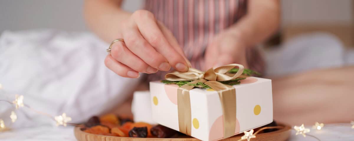 A person unwraps a gift box labelled Healthy Snack Gift Ideas, surrounded by dried fruits and fairy lights on the bed. | Emping SG