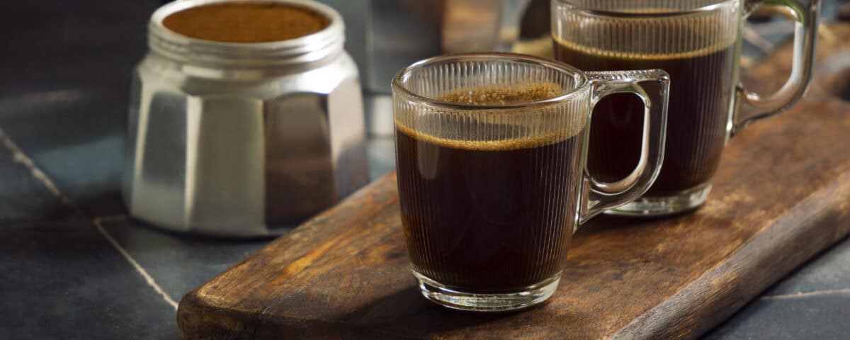 Two glass mugs of fresh roasted coffee on a wooden board beside a moka pot and open coffee tin. | Emping SG
