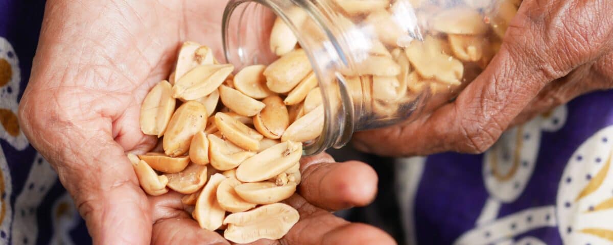 A person pours dried seeds or nuts from a glass jar into their hand over a patterned fabric background. | Emping SG