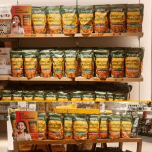 Emping Melinjo Crisps (Lime Leaf) by Emping So Good are neatly stacked on three Harvest Eatery shop display shelves. | Emping SG