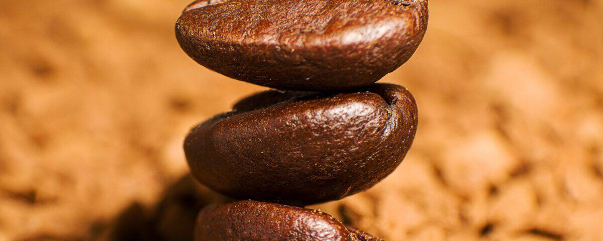 Three coffee beans stacked vertically atop a bed of instant coffee granules. | Emping SG