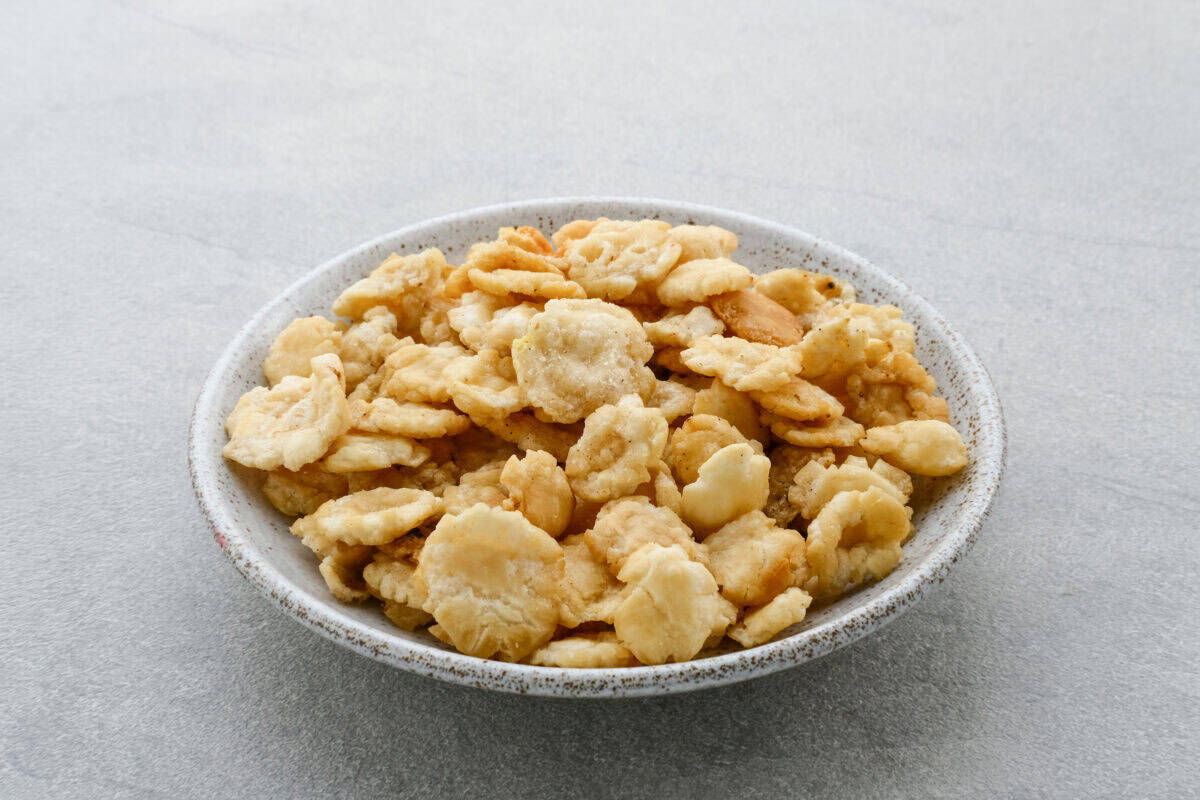 A bowl filled with crispy, golden fried Emping Melinjo chips on a light gray surface. | Emping SG