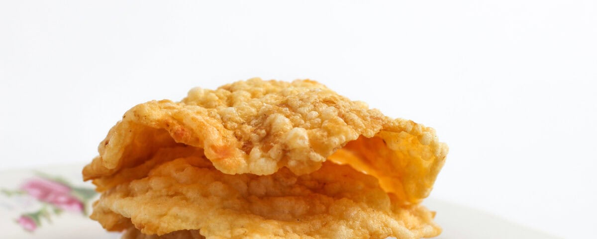 A stack of crispy fried crackers—a tasty treat—on a floral-patterned plate against a white background. | Emping SG