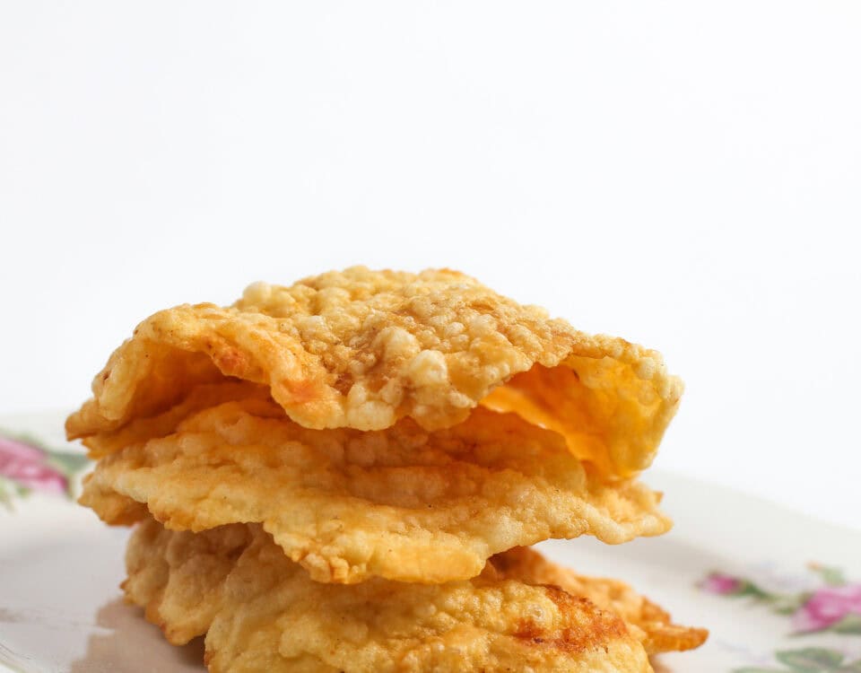 A stack of crispy fried crackers—a tasty treat—on a floral-patterned plate against a white background. | Emping SG