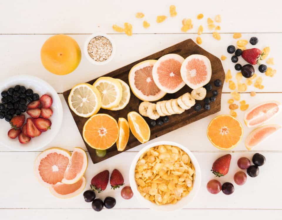 Assorted sliced citrus fruits, berries, and cereal highlight nutrition and ingredients on a white table with a wooden board. | Emping SG