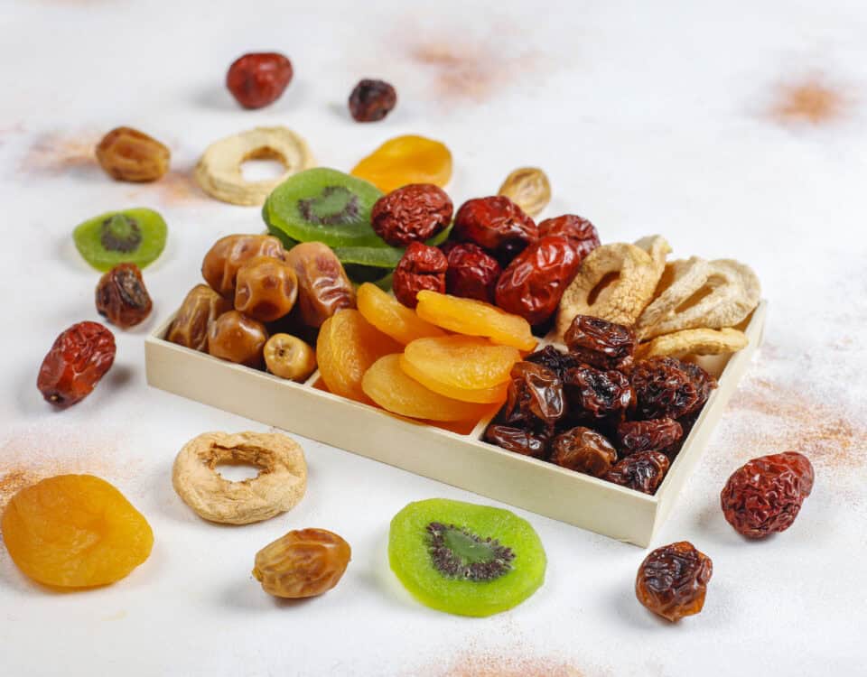 A box of assorted dried fruit snacks—apricots, kiwi, dates, and apples—scattered for healthy snacking tips. | Emping SG