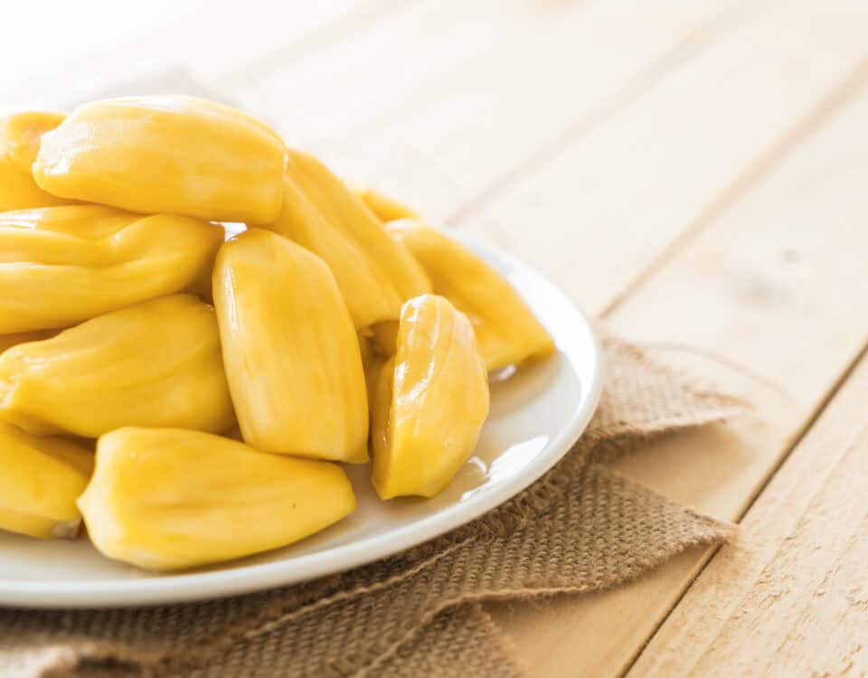 Plate of fresh yellow jackfruit pods, known as Artocarpus heterophyllus, on a white plate atop burlap on a wooden table. | Emping SG