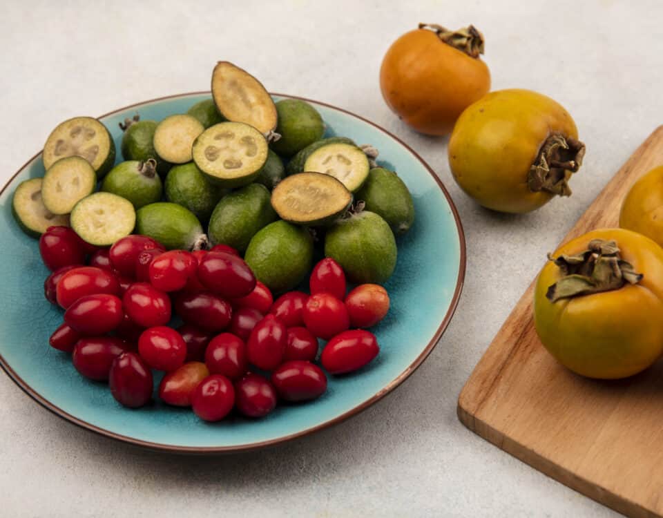A blue plate with feijoas, red berries, and Emping Melinjo crackers next to yellow persimmons on a wooden board. | Emping SG