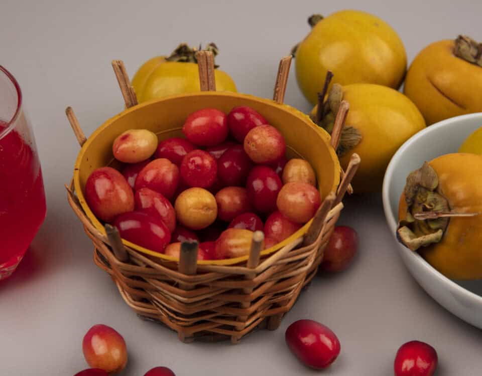 A wicker basket of red cherries, Emping Melinjo chips, and yellow persimmons on a gray surface. | Emping SG
