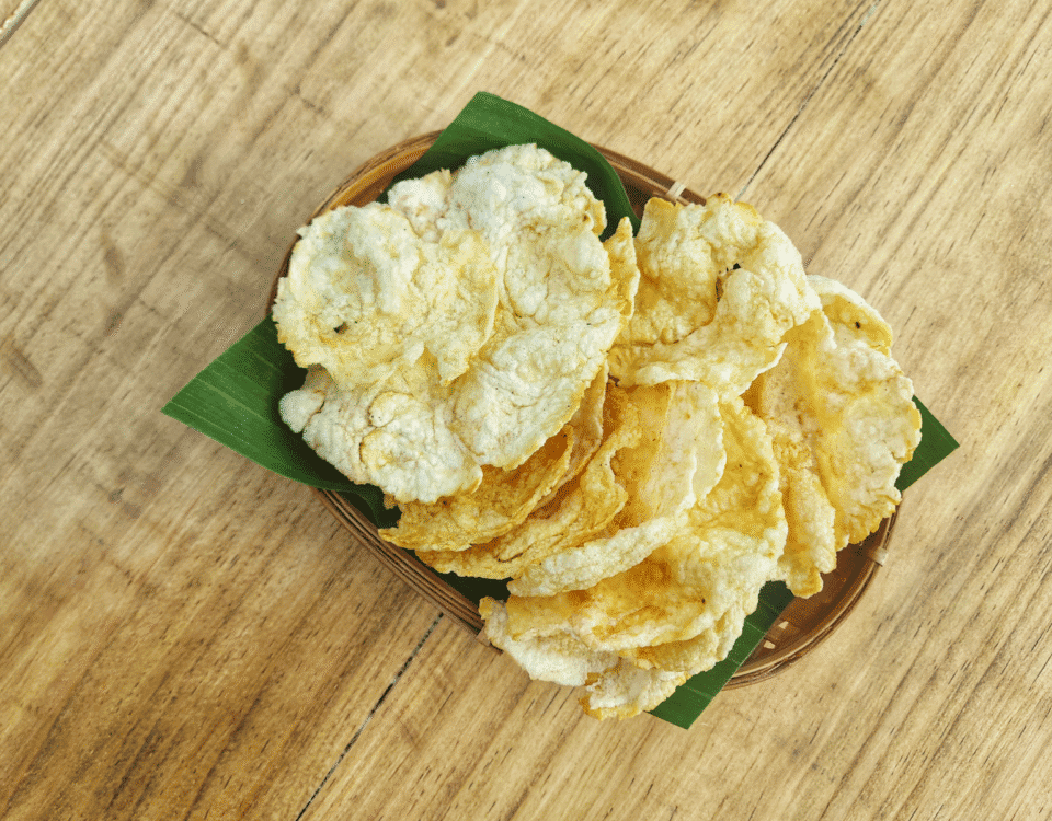 A plate of crispy Emping Crackers with a hint of bitter flavour on a green leaf, placed on a wooden table. | Emping SG