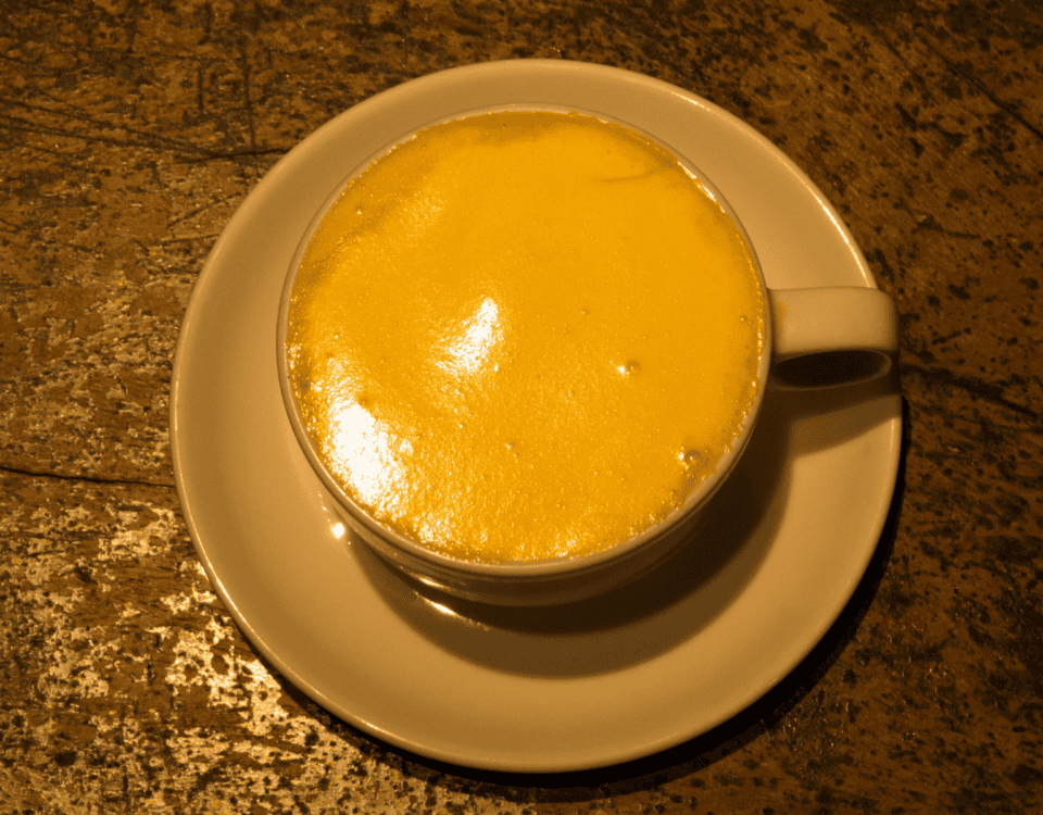A cup of golden yellow Egg Coffee with frothy top, served on a white saucer in Hanoi Old Quarter. | Emping SG