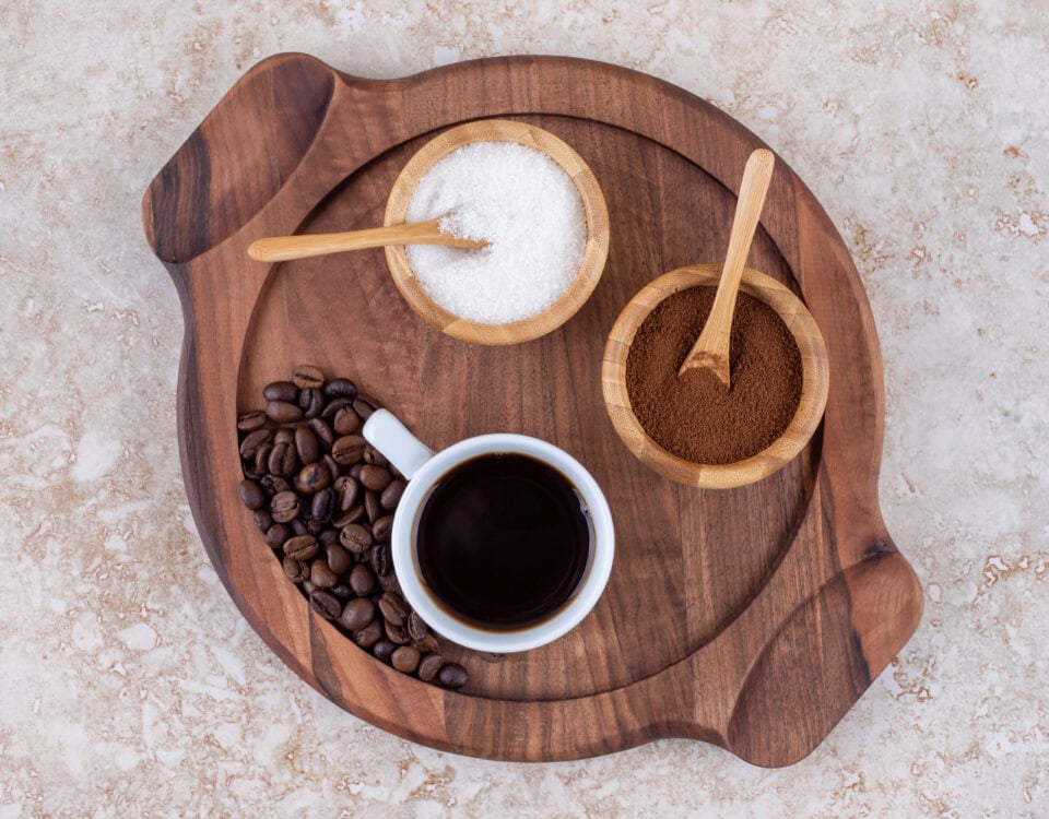 Cup of black coffee, coffee beans, sugar, and ground coffee on a wooden tray—explore the health benefits from above. | Emping SG
