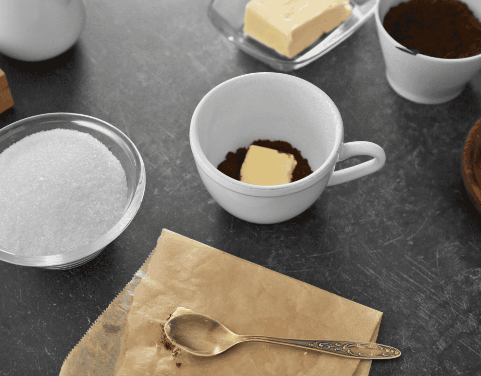 A cup with cocoa powder and butter, a bowl of sugar, and baking ingredients on a dark worktop. | Emping SG